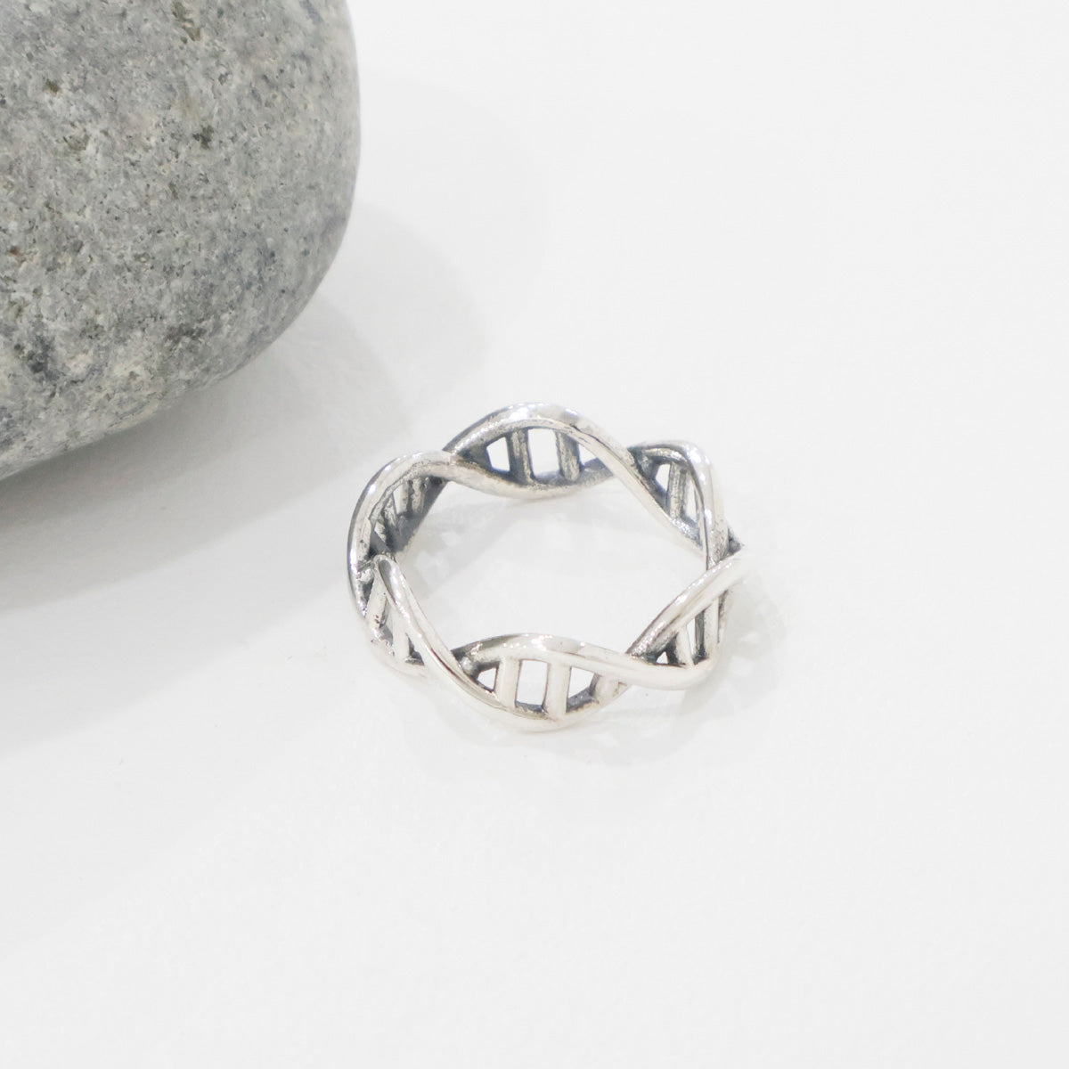 Openwork sterling silver DNA band ring placed beside a round grey stone on a white background.