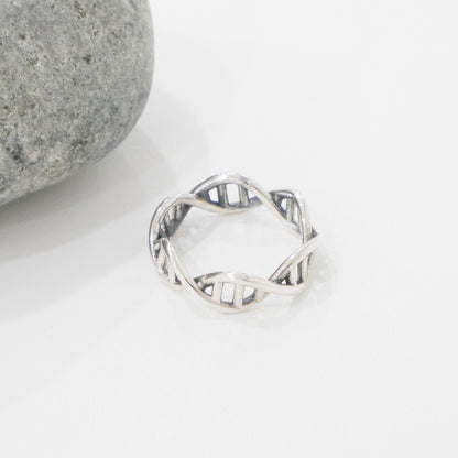 Openwork sterling silver DNA band ring placed beside a round grey stone on a white background.