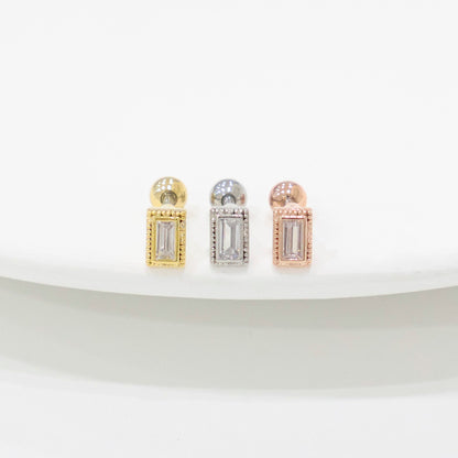 Three rectangular CZ barbell earrings in clear stones, displayed in gold, silver, and rose gold settings on a white curved surface.