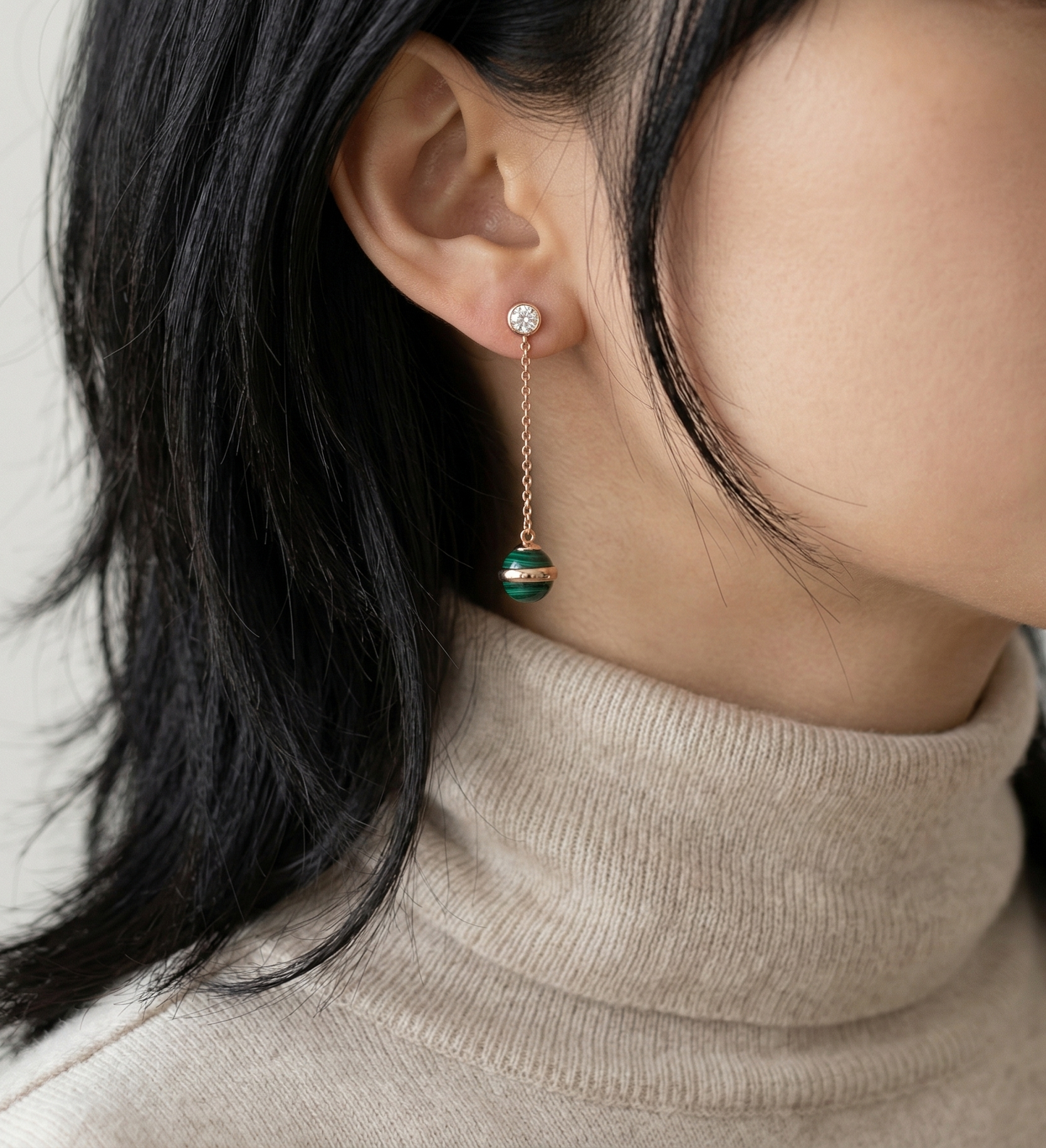 Model wearing natural malachite chain drop earrings with long dark hair over a beige turtleneck, earring shown close to face from front angle