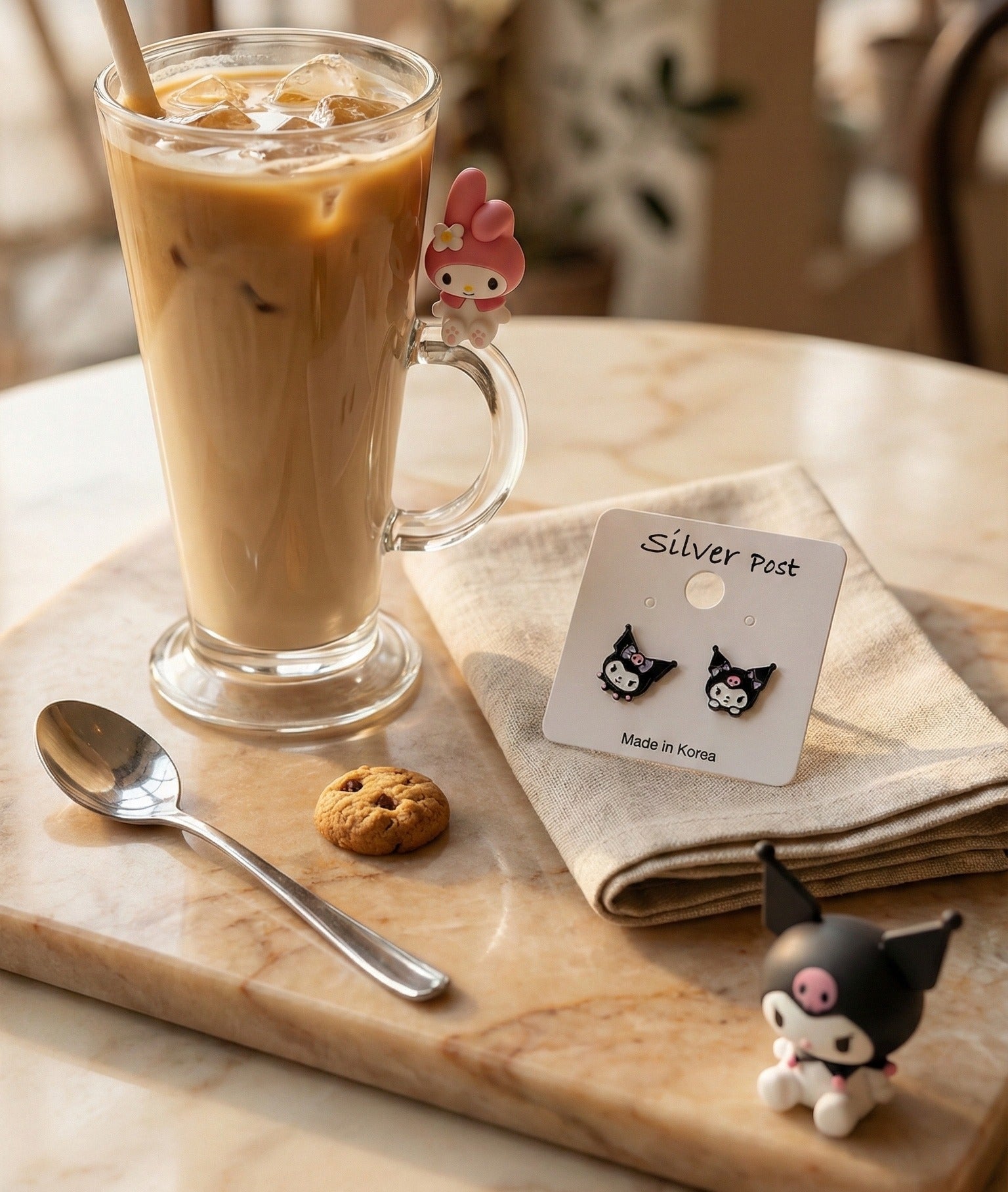 Close-up lifestyle shot of Kuromi stud earrings next to latte glass and My Melody figure