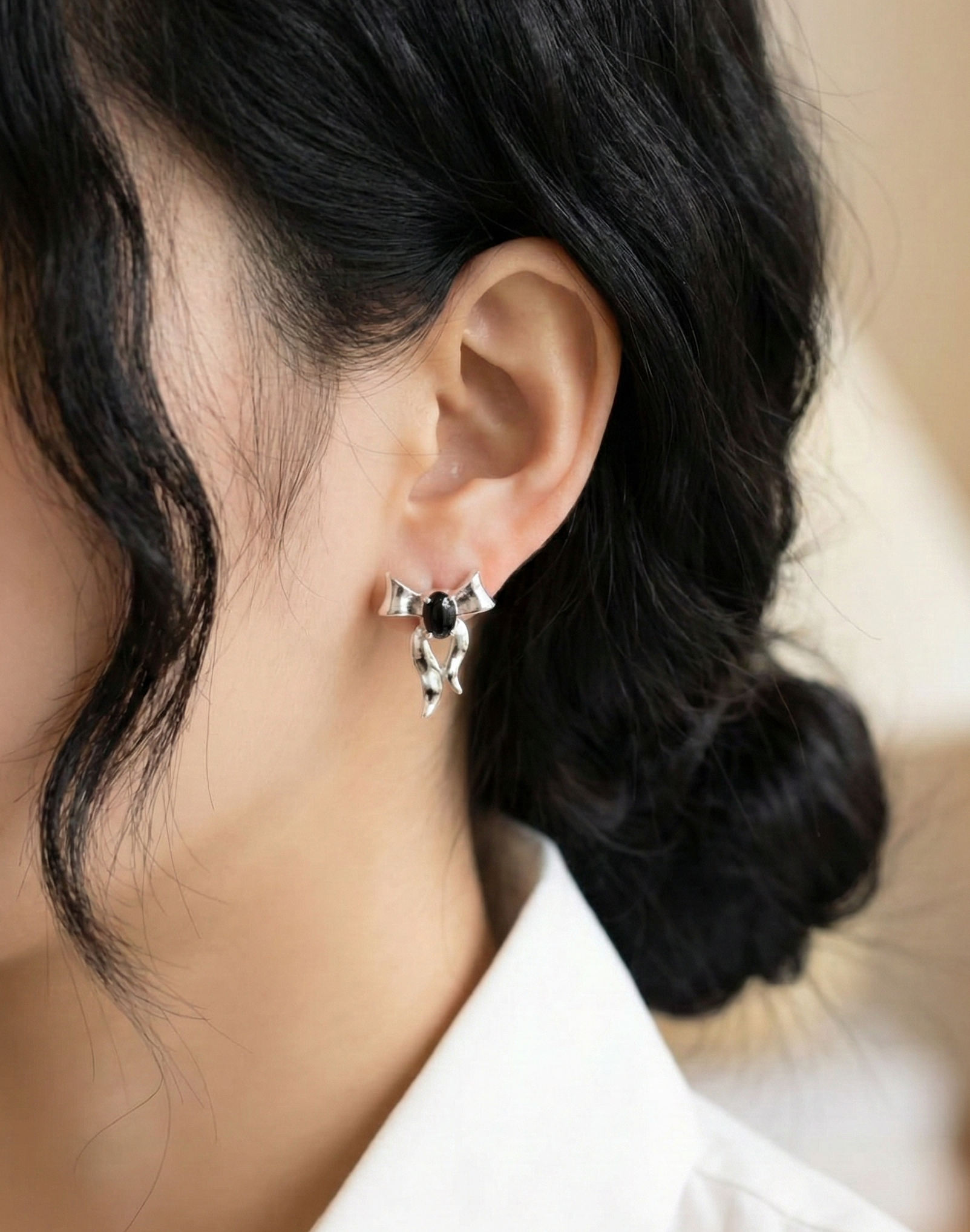 Korean woman with dark updo hair wearing silver bow earrings with black agate stone — white blazer styling, 