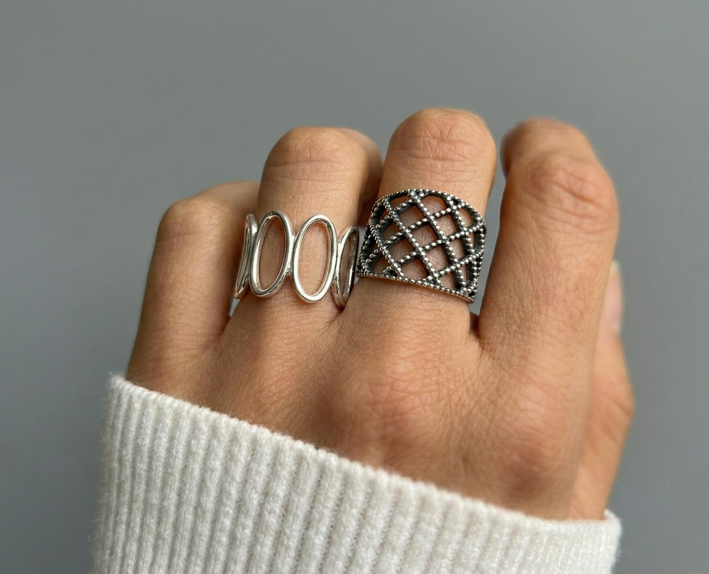 Model wearing 925 sterling silver oval loop ring and lace lattice ring together on two fingers, white ribbed knit sleeve, mix-and-match bold ring stack