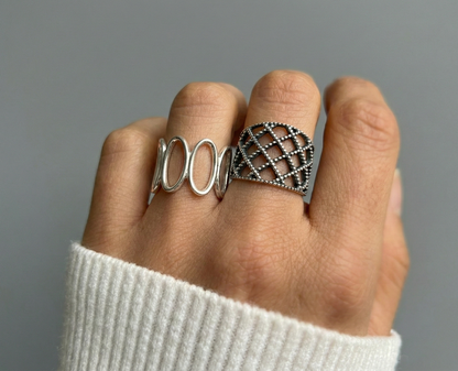 Model wearing 925 sterling silver oval loop ring and lace lattice ring together on two fingers, white ribbed knit sleeve, mix-and-match bold ring stack
