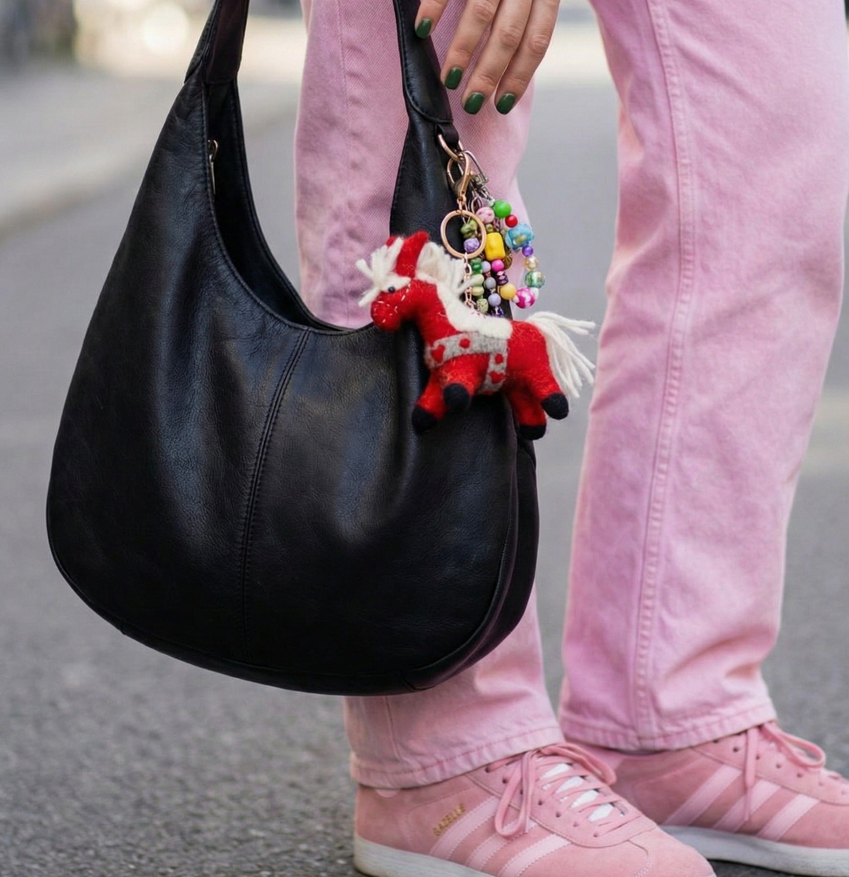 Woman in pink outfit holding black hobo bag with red horse felt bag charm and colorful beaded keyring