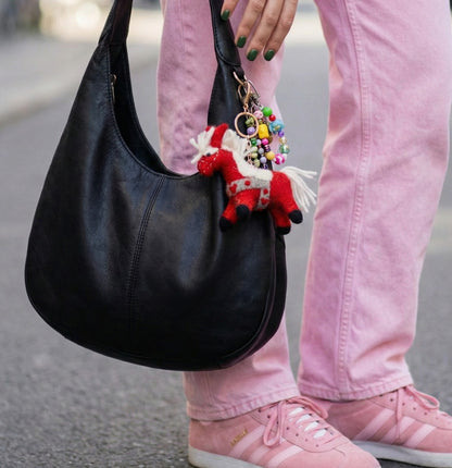 Woman in pink outfit holding black hobo bag with red horse felt bag charm and colorful beaded keyring