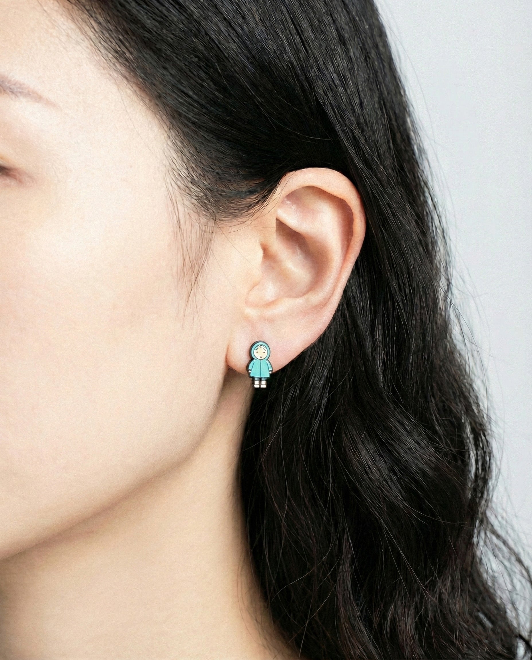 Close-up of blue raincoat Mei character stud earring on model's earlobe