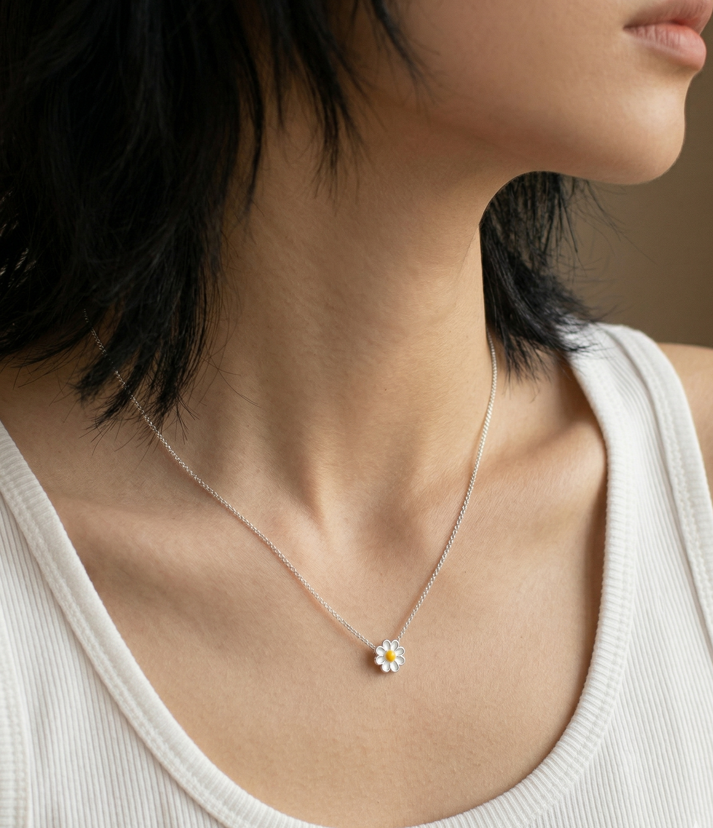 Woman wearing 925 sterling silver daisy pendant necklace on collarbone, styled with a white ribbed tank top, side profile close-up