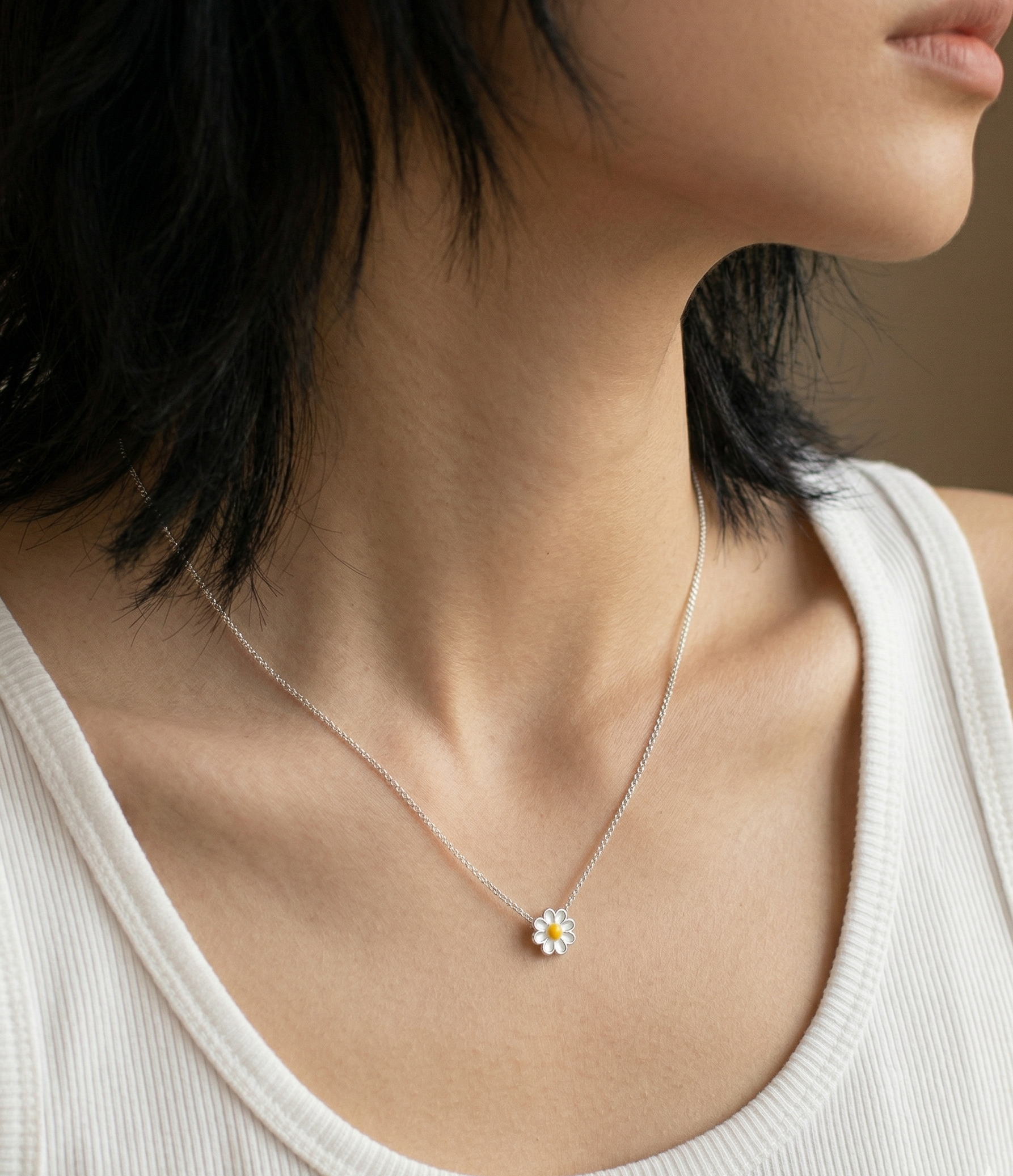 Woman wearing 925 sterling silver daisy pendant necklace on collarbone, styled with a white ribbed tank top, side profile close-up