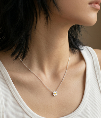 Woman wearing 925 sterling silver daisy pendant necklace on collarbone, styled with a white ribbed tank top, side profile close-up