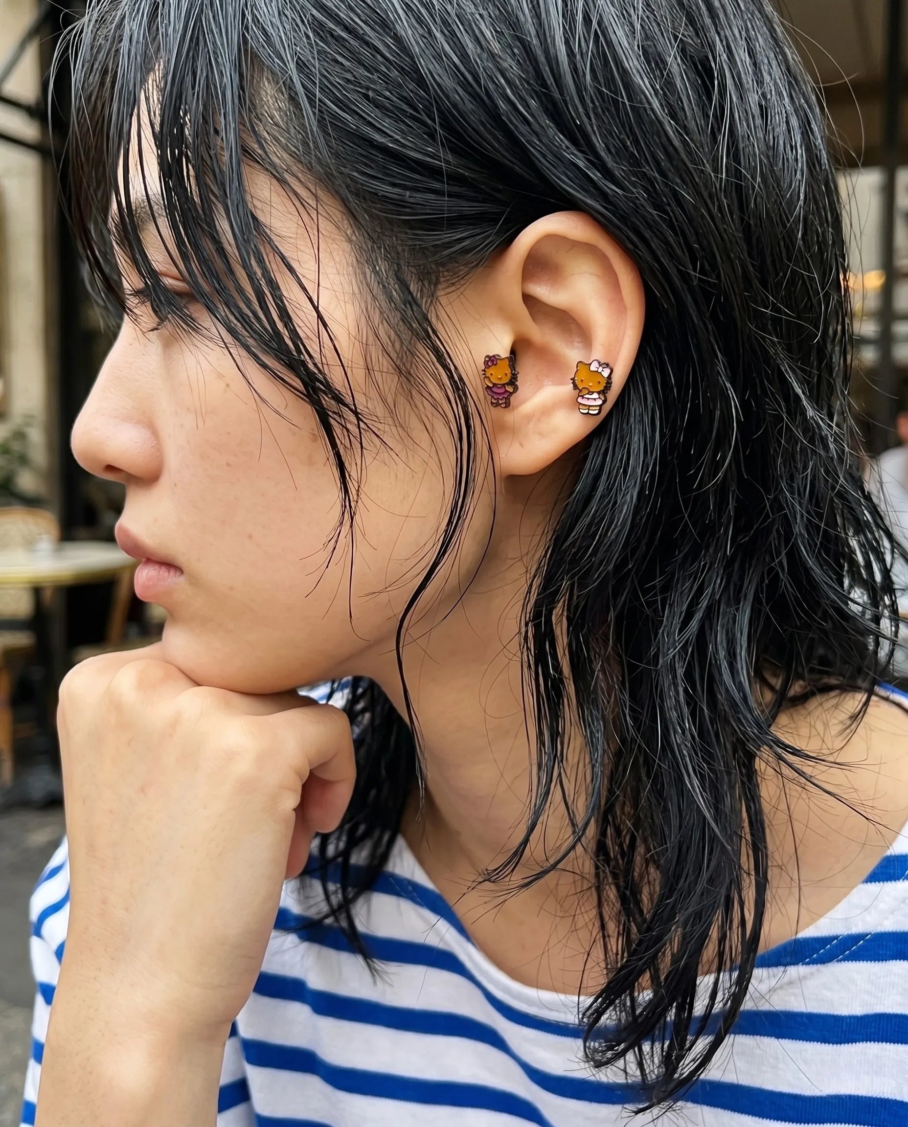 K-fashion curated ear inspo featuring Hello Kitty tanning piercing — grunge shaggy layered hair, striped tee, inner conch and lobe double piercing stack.
