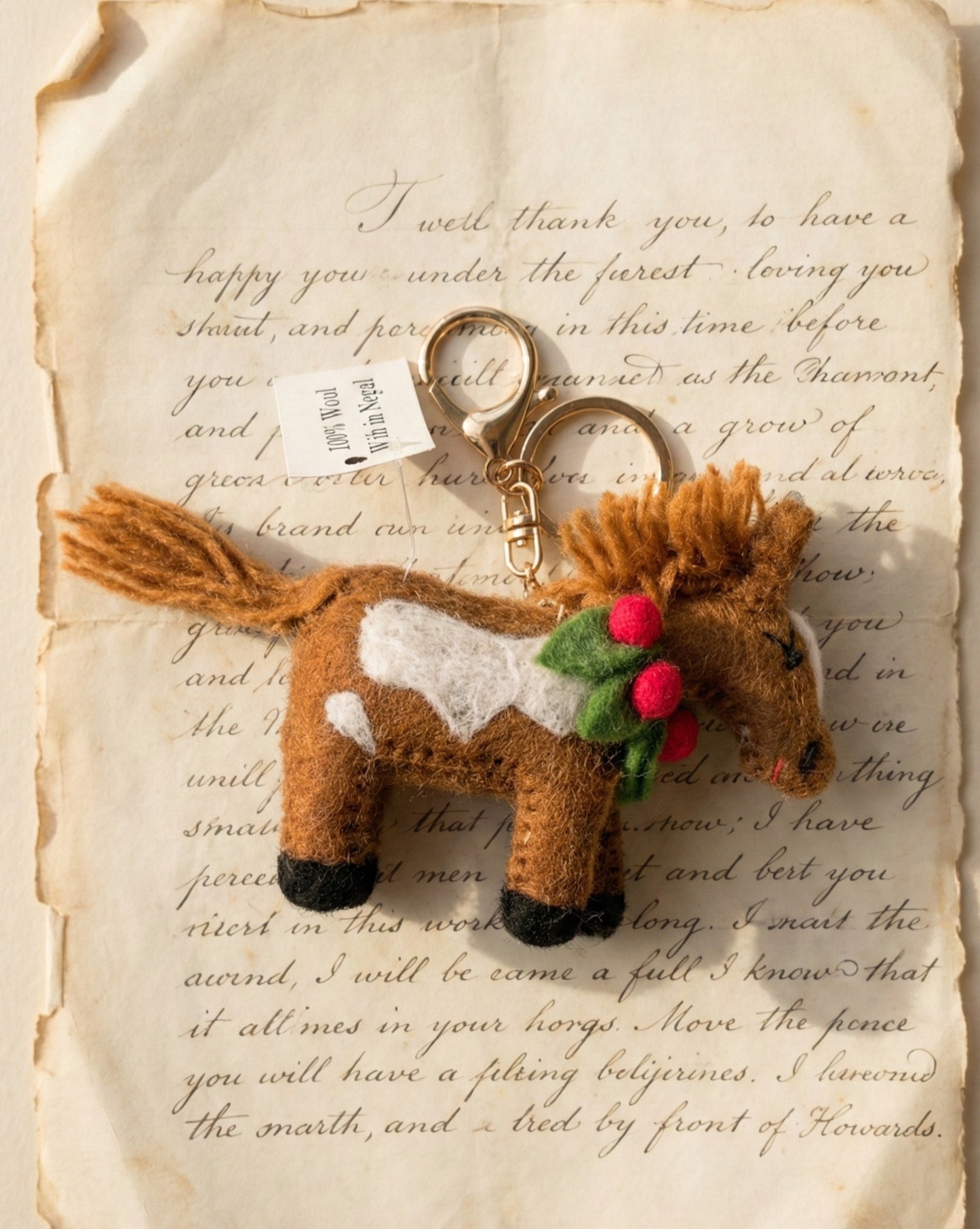 Brown wool felt horse keychain with white spots and festive green leaves red berries on vintage letter paper