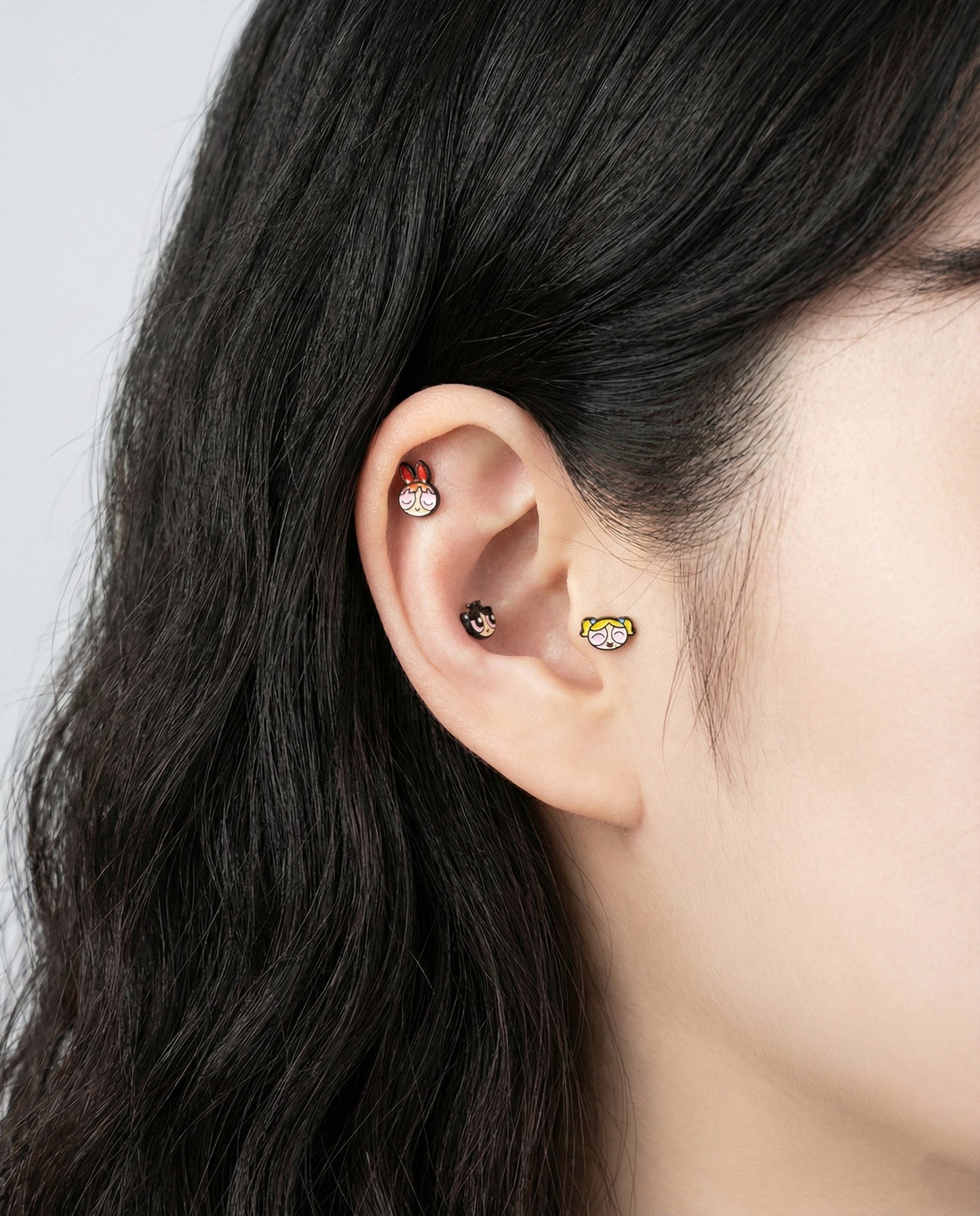  Woman wearing two Powerpuff Girls sleeping stud earrings on earlobe - Blossom and Bubbles brass enamel surgical steel