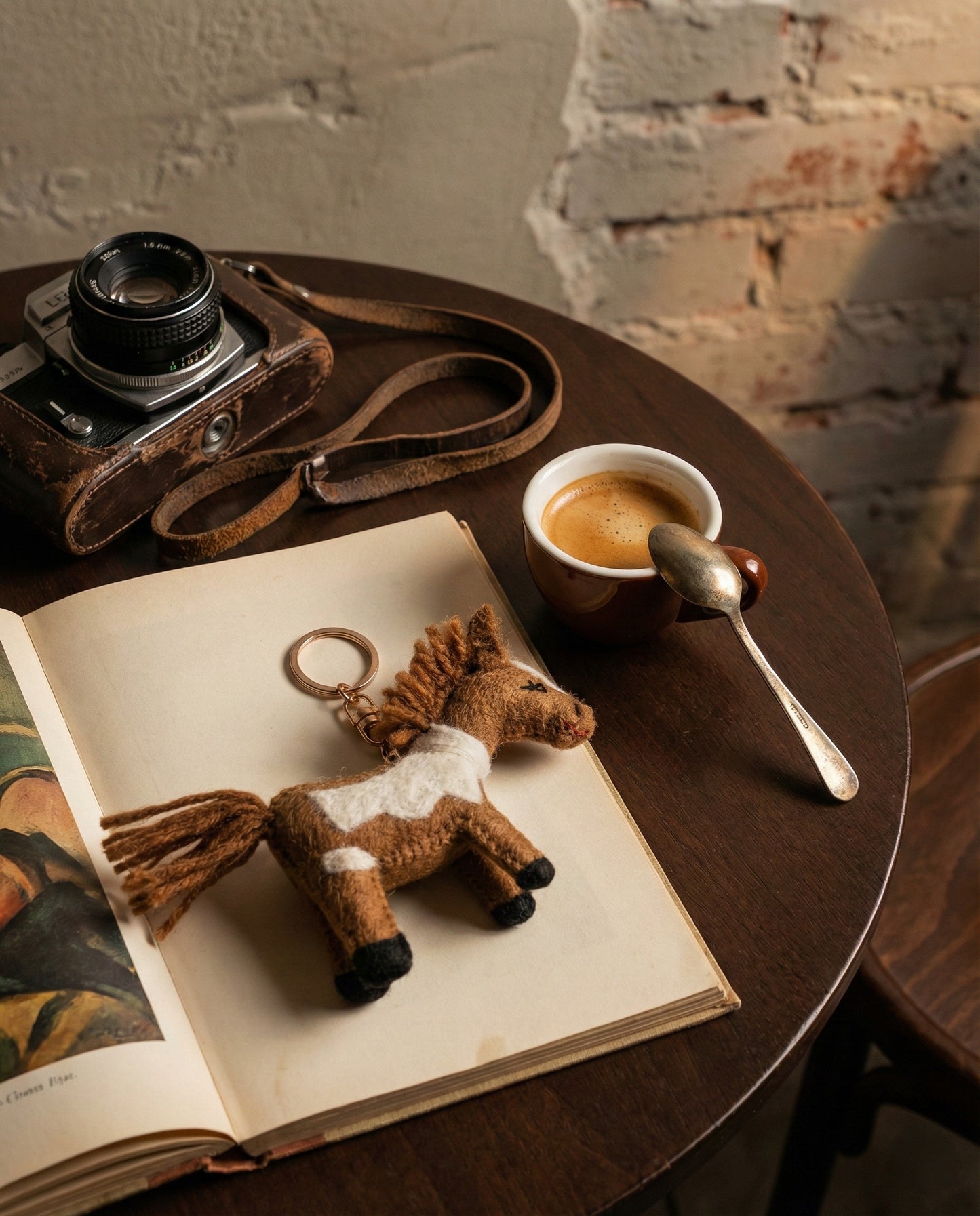 Brown handmade felt horse keychain on vintage book with espresso cup and retro camera