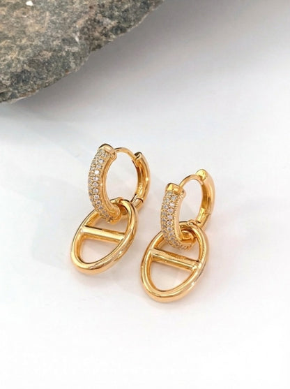 Close-up of gold pavé cubic zirconia huggie earrings with anchor charm drop