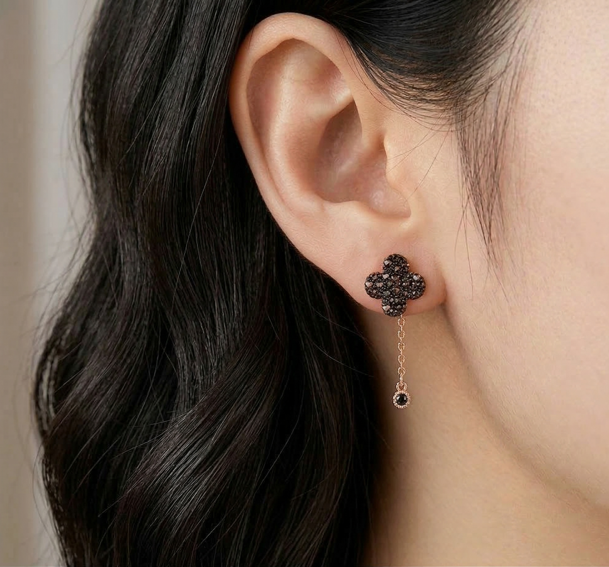 Close-up side profile of cognac pavé clover earring worn with rose gold chain drop dangling below earlobe, dark hair background