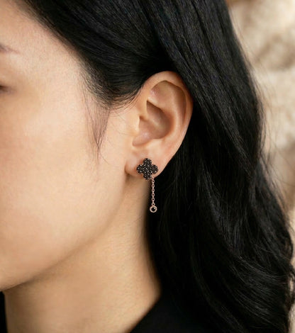 Close-up of a person wearing a dangling earring with a dark stone and chain.