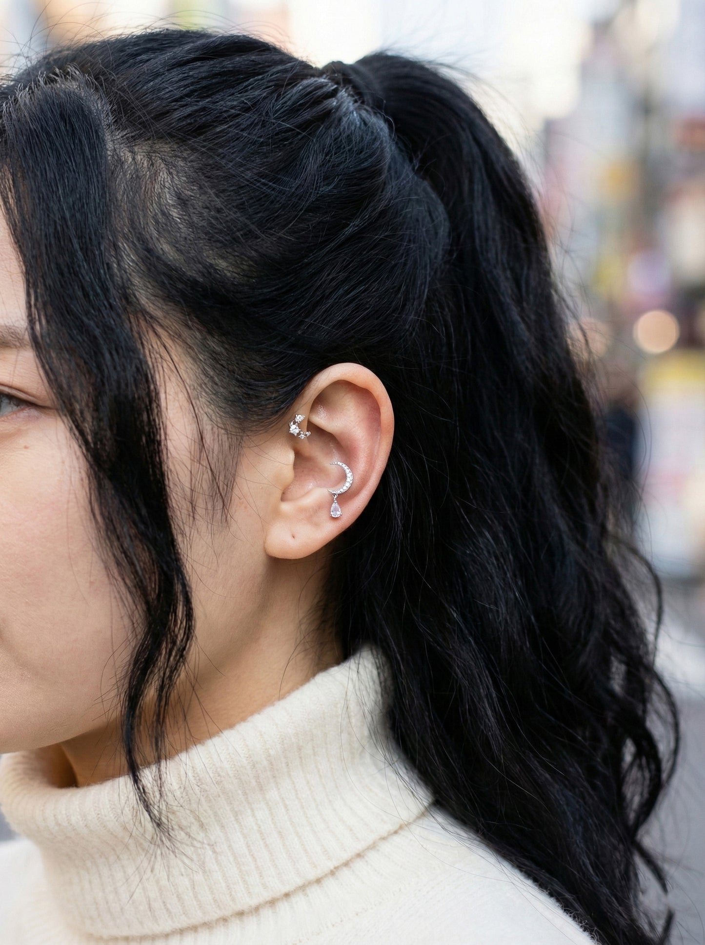 Close-up of sparkling cubic zirconia crescent moon with pear-cut teardrop dangle on ear cartilage