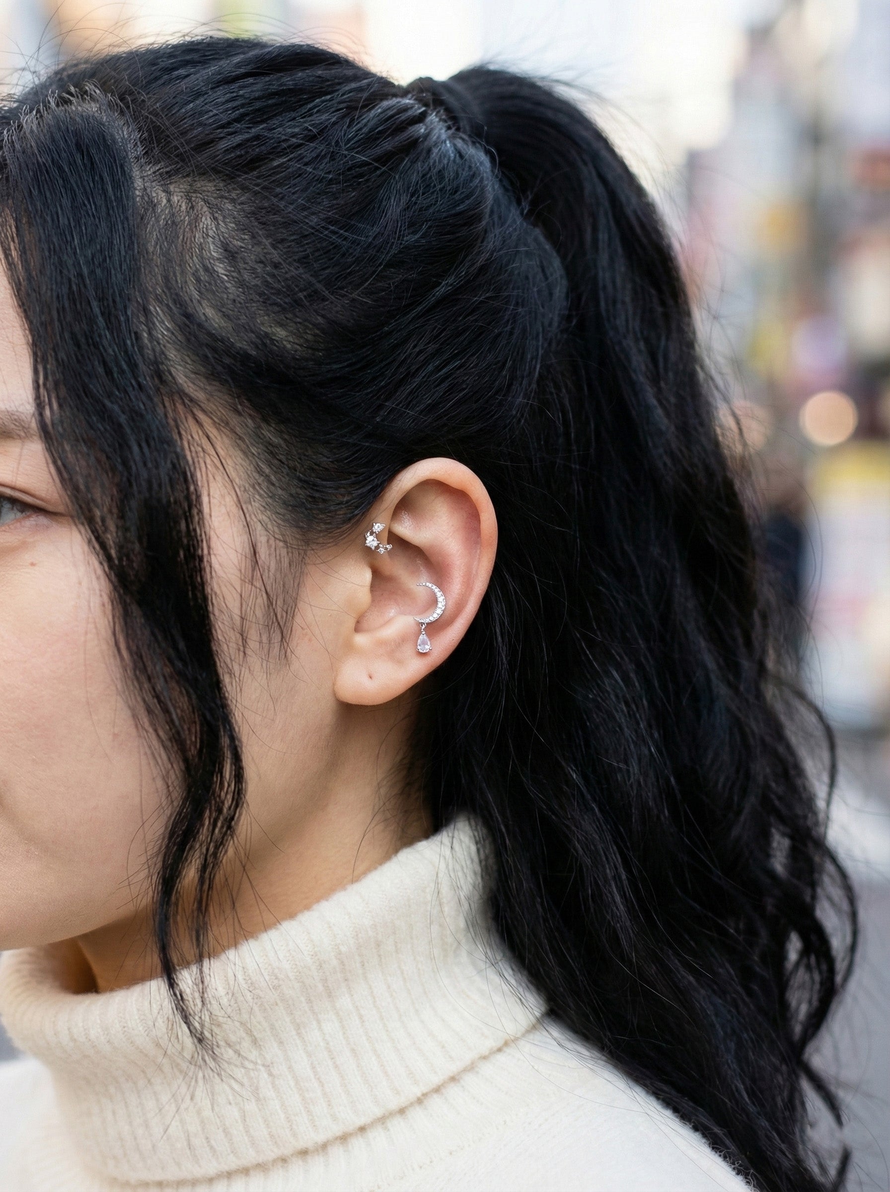 Close-up of sparkling cubic zirconia crescent moon with pear-cut teardrop dangle on ear cartilage