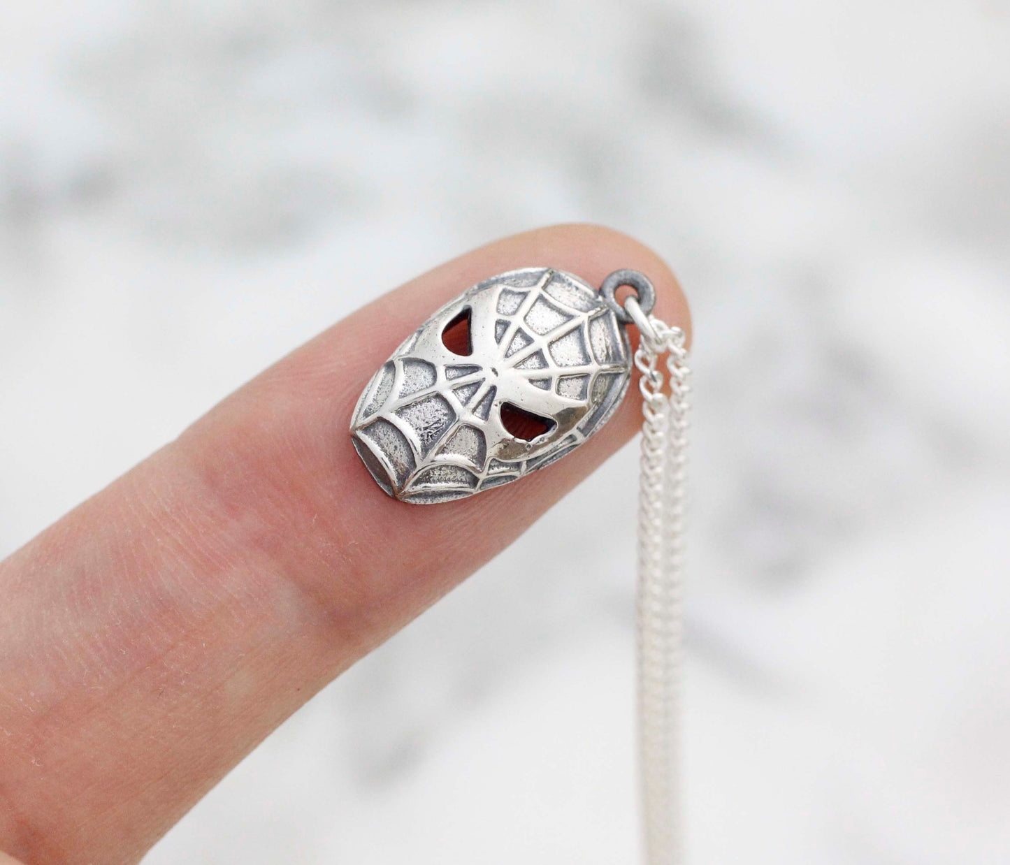 Hand holding a small 1x2cm unique silver spider pendant showing handmade texture