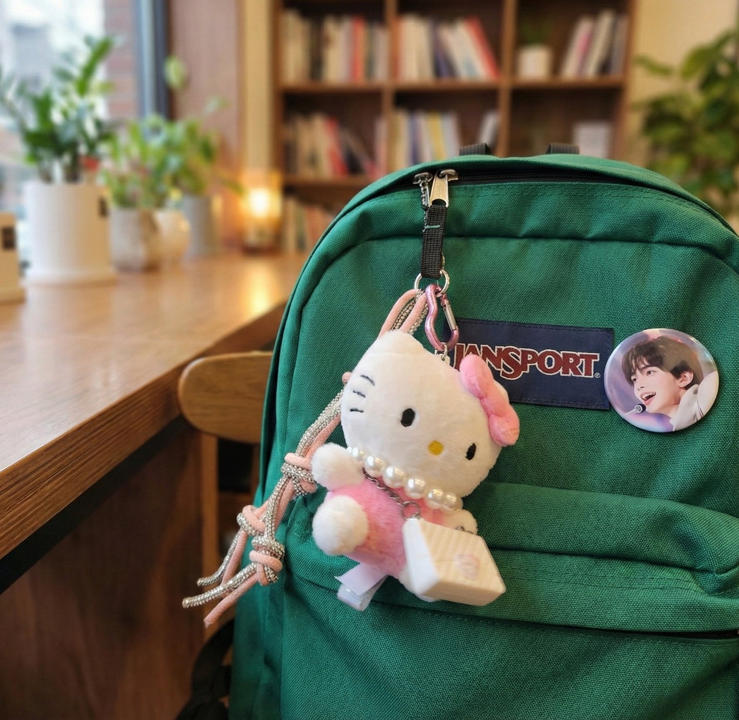 Hello Kitty plush keychain attached to a green Jansport backpack in a cozy study room setting — kawaii bag charm for school