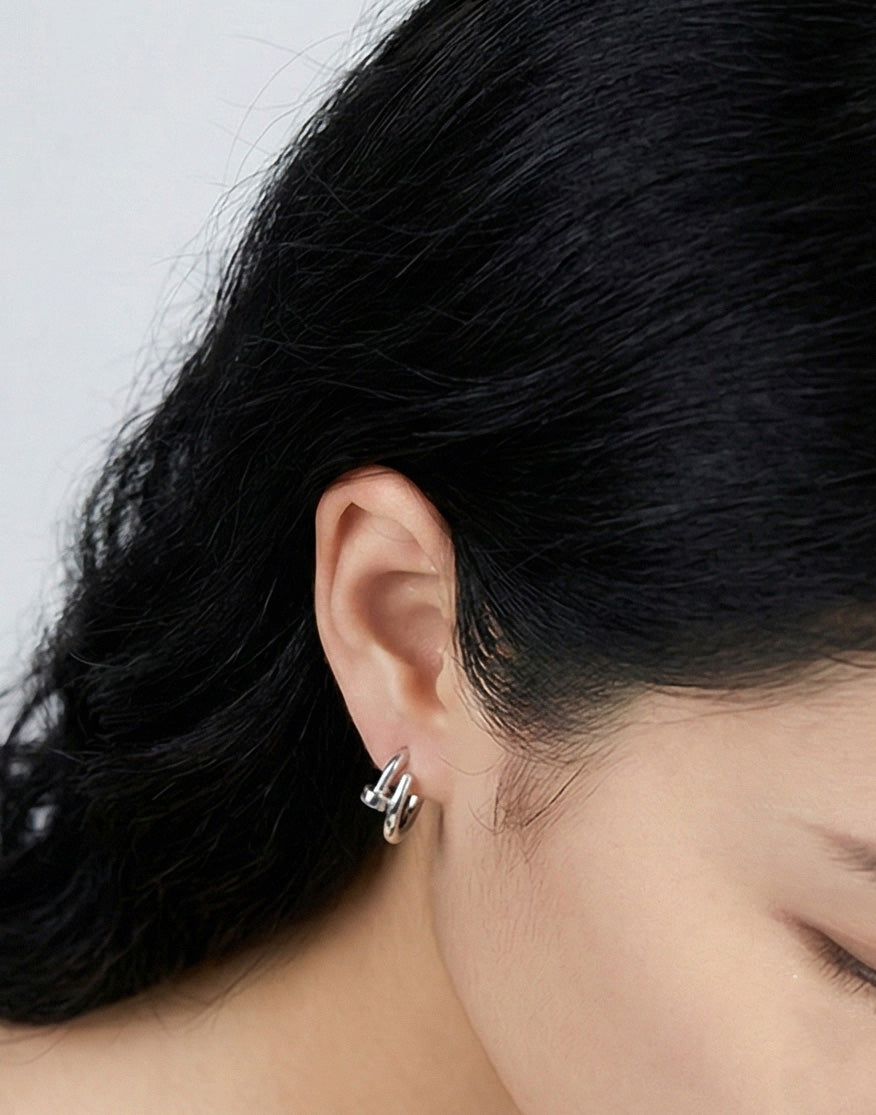 Close-up side view of silver hoop earrings layered on ear.
