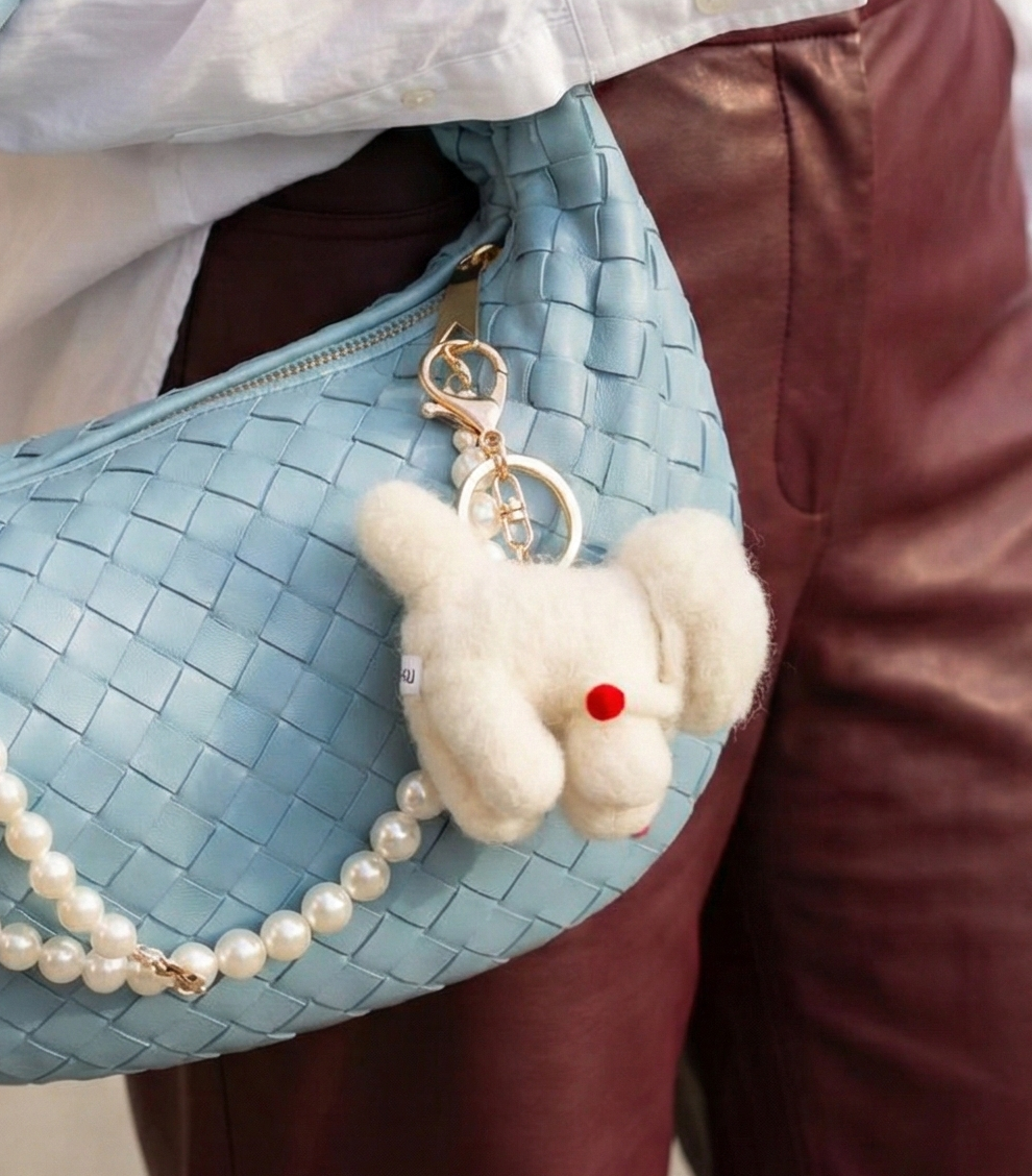 Close-up of Bichon keychain on bag zipper with gold-tone hardware
