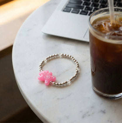 Pink Hug Me gummy bear acrylic charm 925 silver beaded bracelet on marble cafe table next to iced Americano and laptop