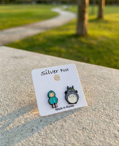 Totoro and Mei earrings on white card labeled Silver Post against green park background