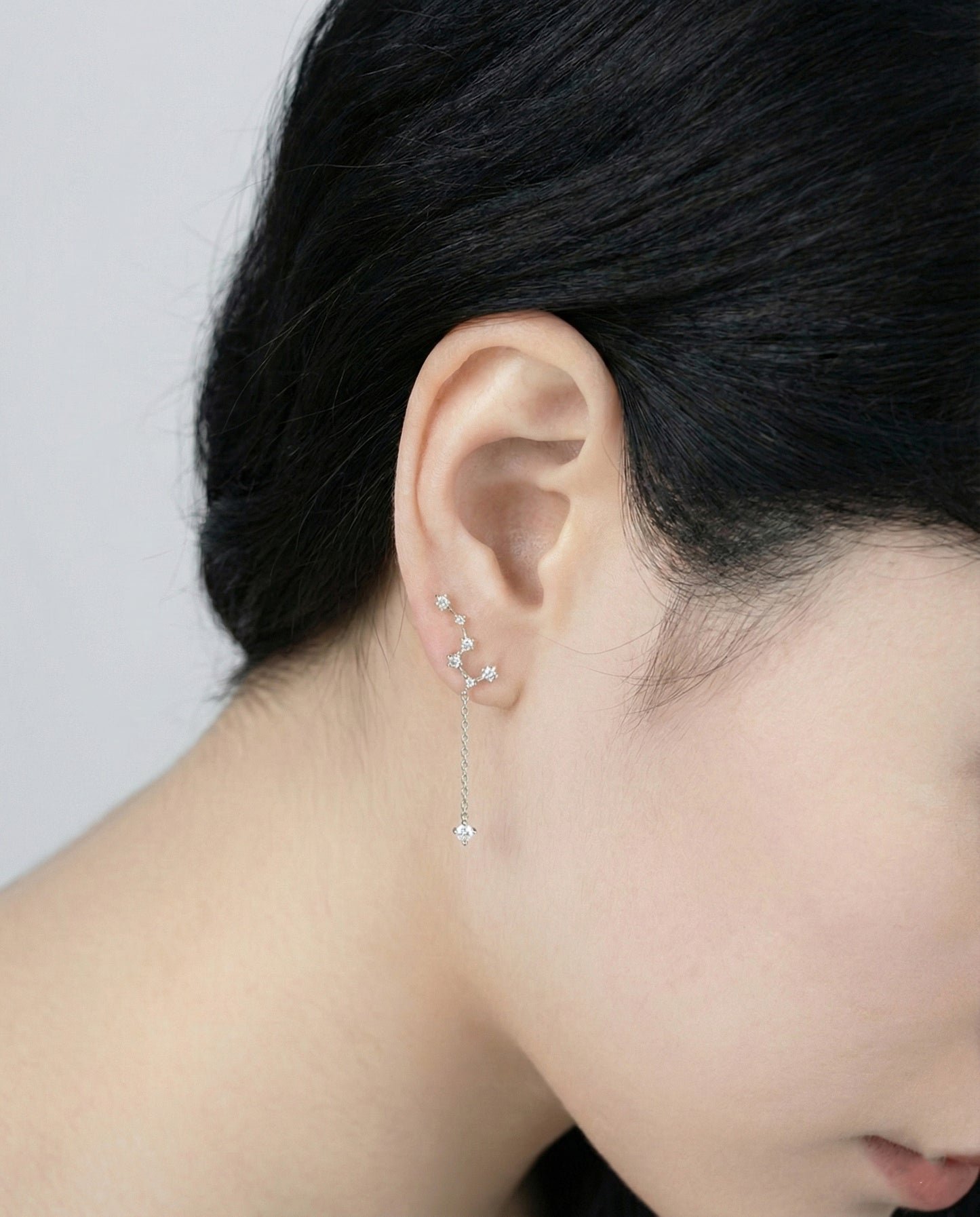 Close-up profile of woman wearing silver constellation earring on ear, showing cascading cubic zirconia star design with chain drop, 925 silver hypoallergenic posts, minimalist everyday jewelry