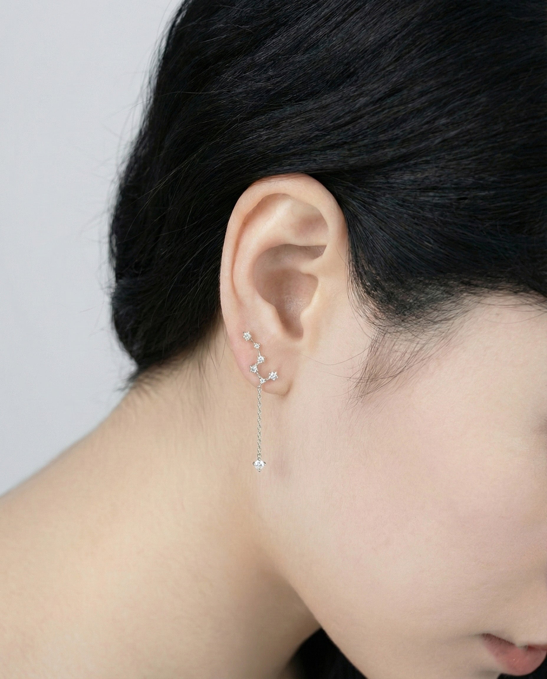 Close-up profile of woman wearing silver constellation earring on ear, showing cascading cubic zirconia star design with chain drop, 925 silver hypoallergenic posts, minimalist everyday jewelry