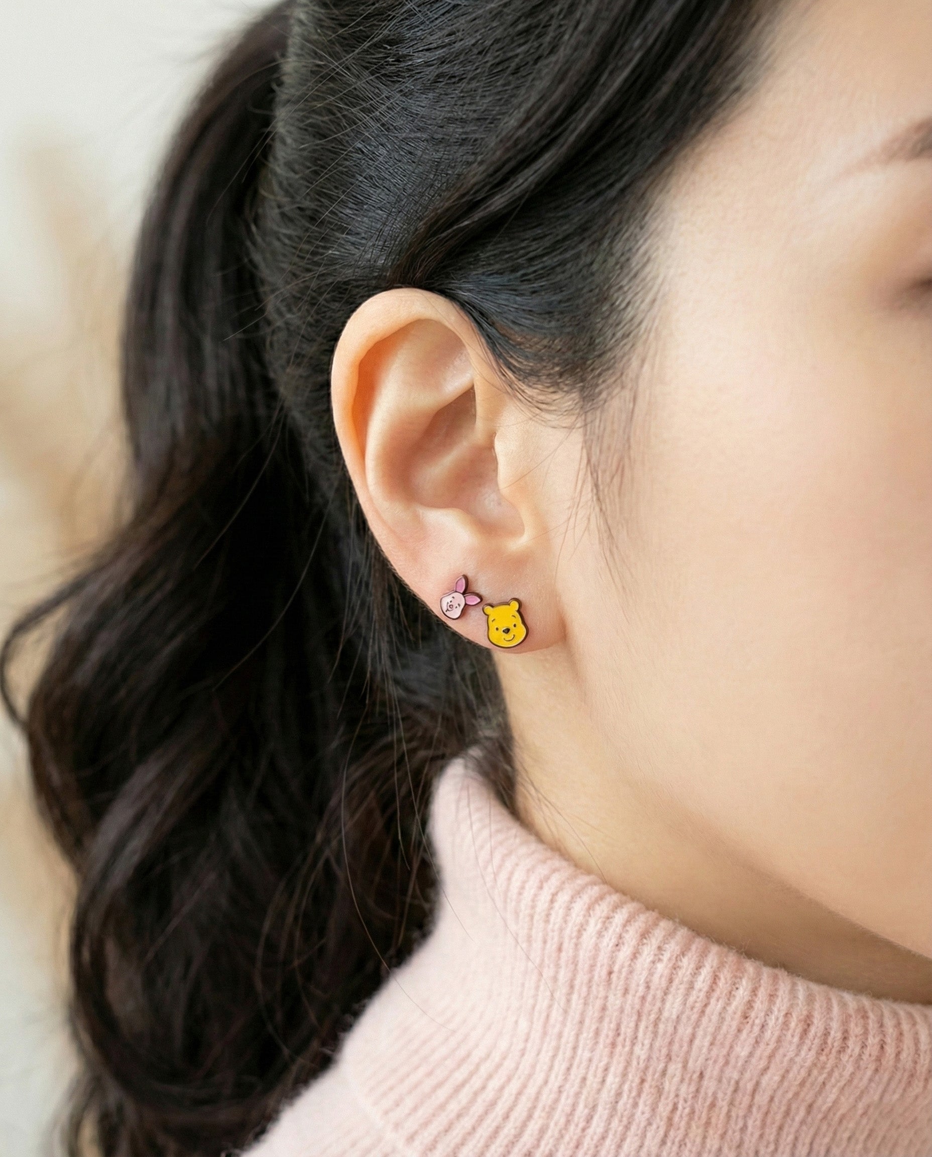 Model wearing Winnie the Pooh and Piglet mismatched stud earrings in pink sweater
