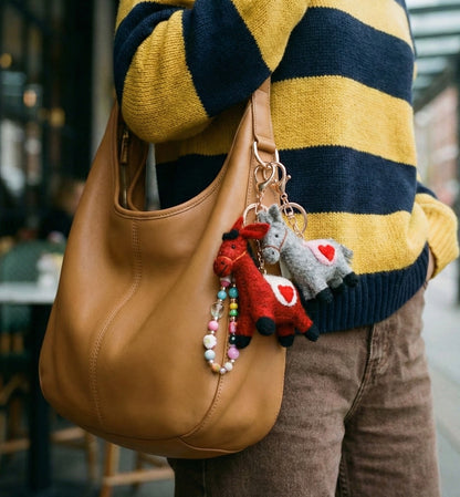 Red and grey felt pony bag charms clipped on tan leather hobo bag worn with striped sweater