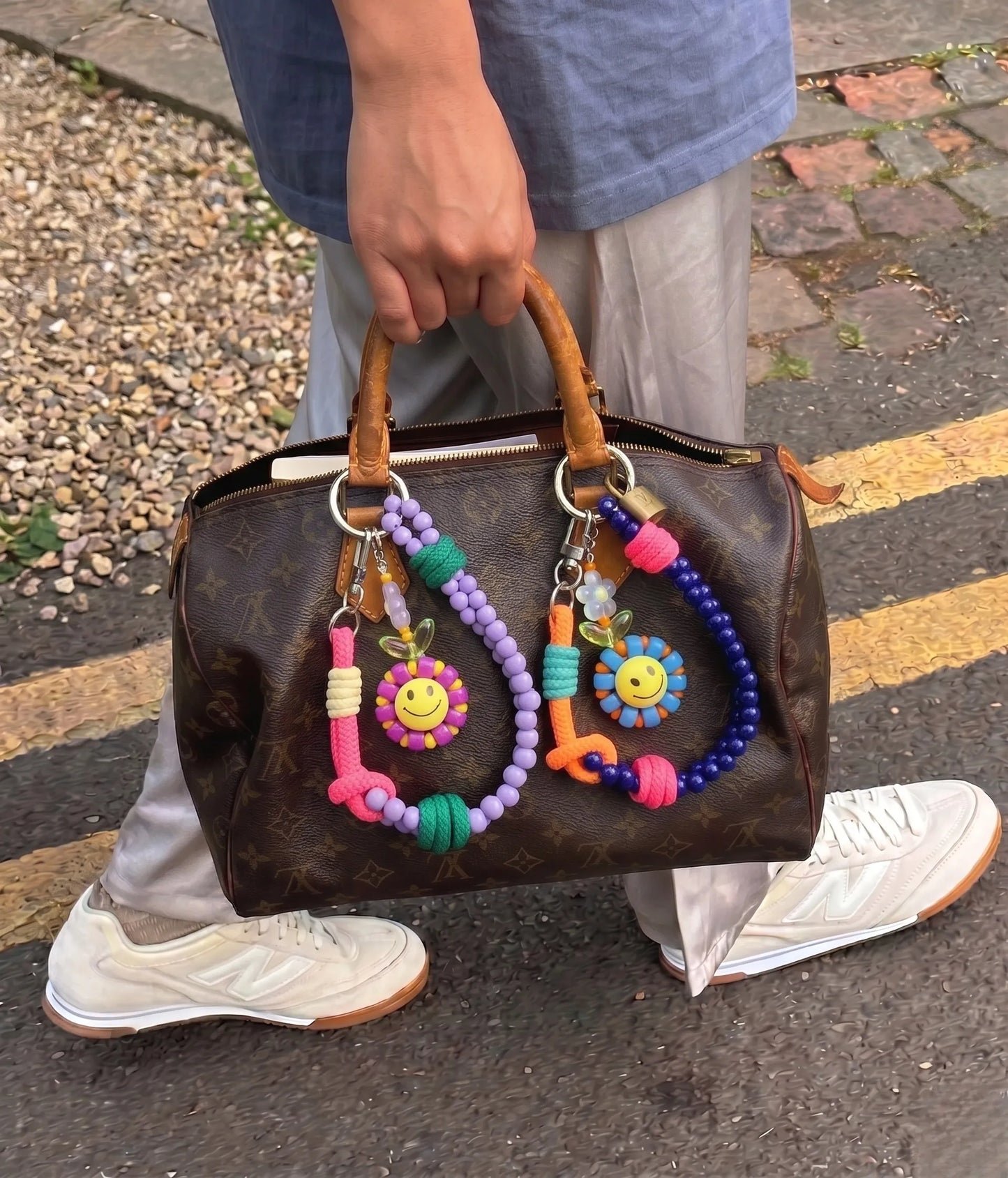 Street style bag charm inspo 8ttitto8 smiley flower beaded keychain on Louis Vuitton Speedy, Y2K kidcore layered look with New Balance sneakers.