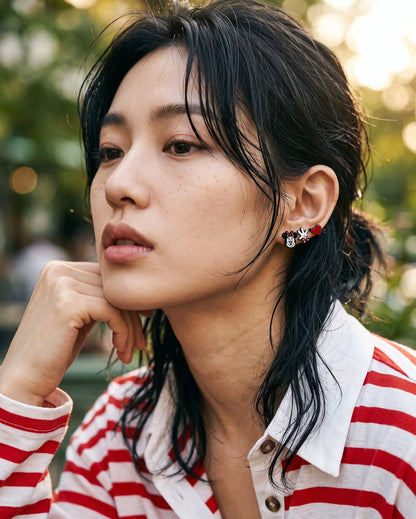 Model wearing mismatched mouse stud earrings in curated ear stack, red striped shirt, layered cut hair.