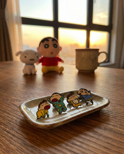 Shin-chan and Himawari kawaii earrings displayed on ceramic dish with sunset window background