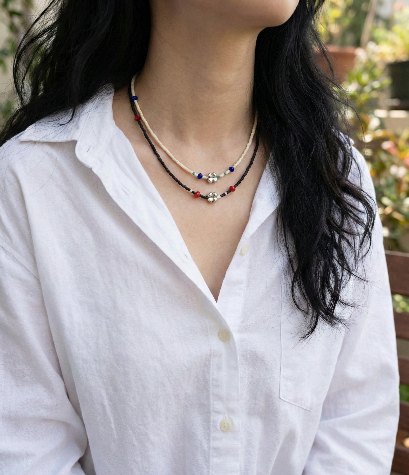 Woman wearing layered ivory and black seed bead choker necklaces with four-leaf clover charms over white shirt
