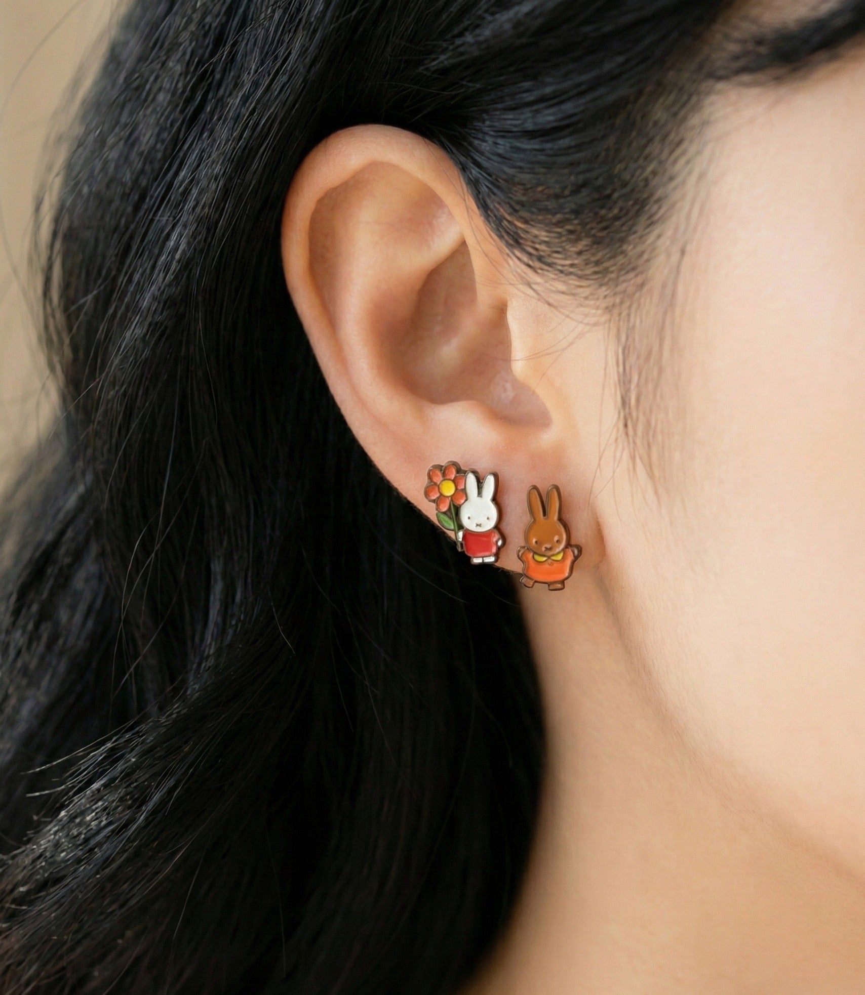 
Side view of mismatched Miffy and Melanie earrings on ear, showing detailed enamel coloring and gold outline finish