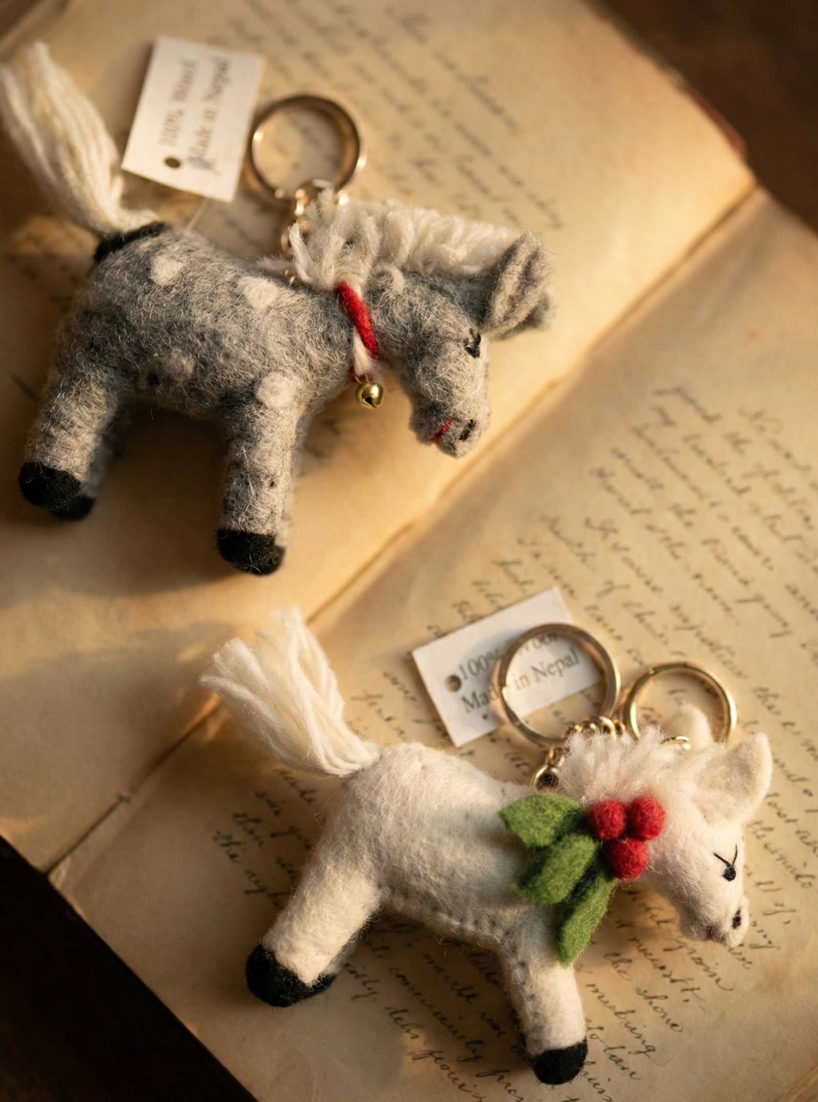 Grey dotted and white wool felt pony keychains with gold bell detail on antique book pages