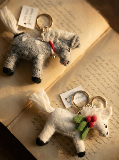Grey dotted and white wool felt pony keychains with gold bell detail on antique book pages