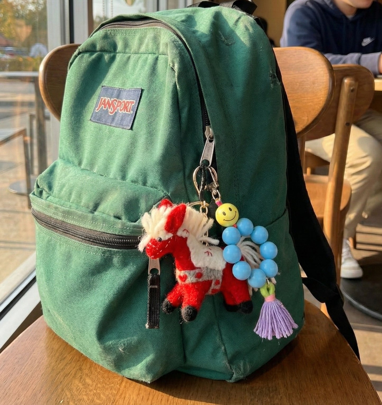 Green Jansport backpack with red horse wool felt keychain, smiley face charm, and blue beads for student bag styling