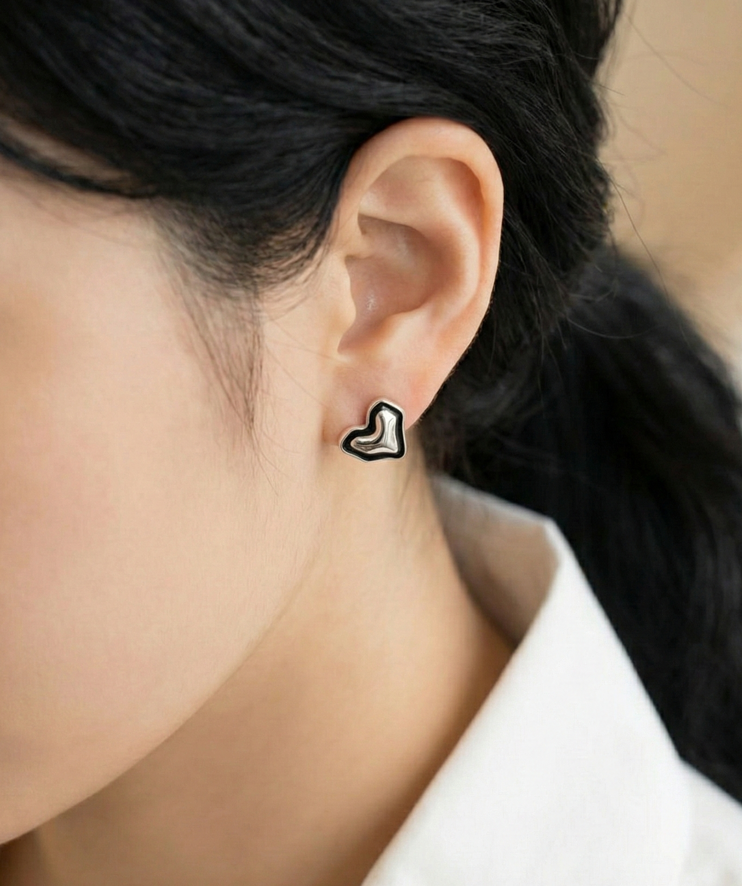 Close-up of organic asymmetric heart stud earring in 925 sterling silver with black enamel outline on woman's ear