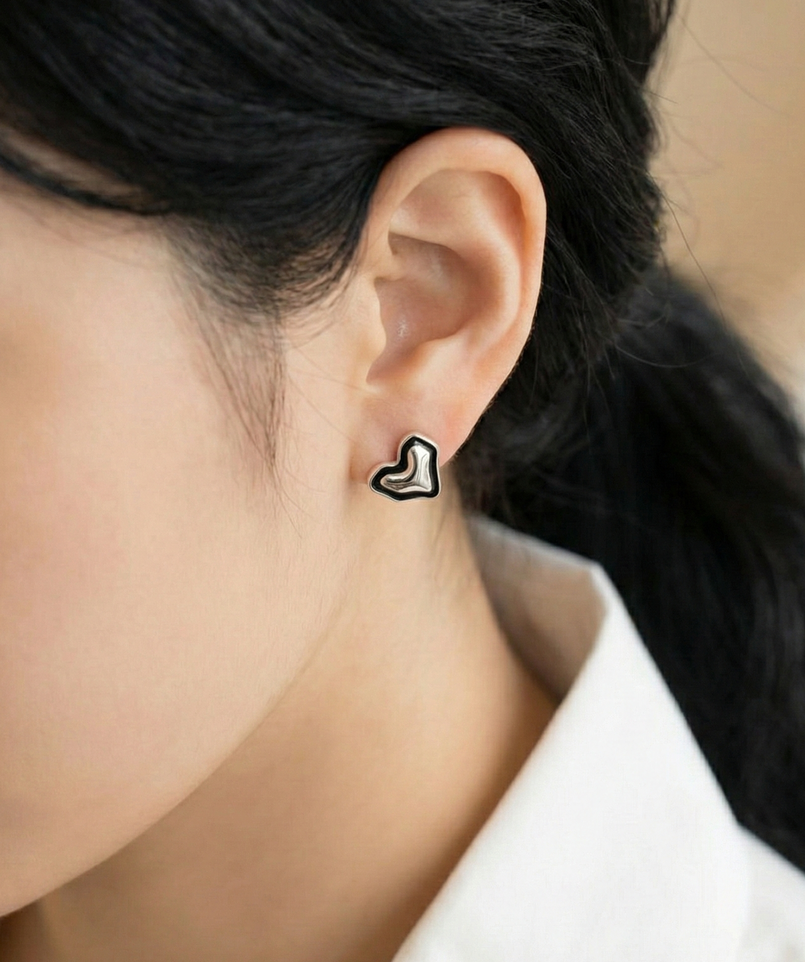 Close-up of organic asymmetric heart stud earring in 925 sterling silver with black enamel outline on woman's ear