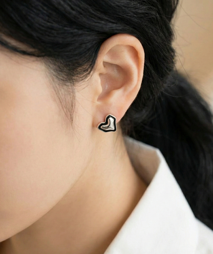 Close-up of organic asymmetric heart stud earring in 925 sterling silver with black enamel outline on woman's ear