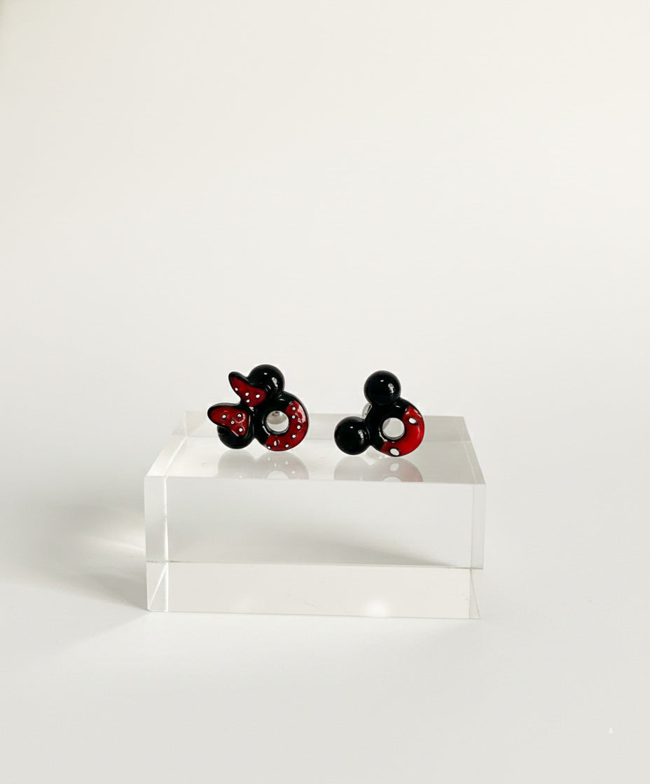 Mismatched Mickey and Minnie Mouse stud earrings displayed on a clear acrylic block against a white background.