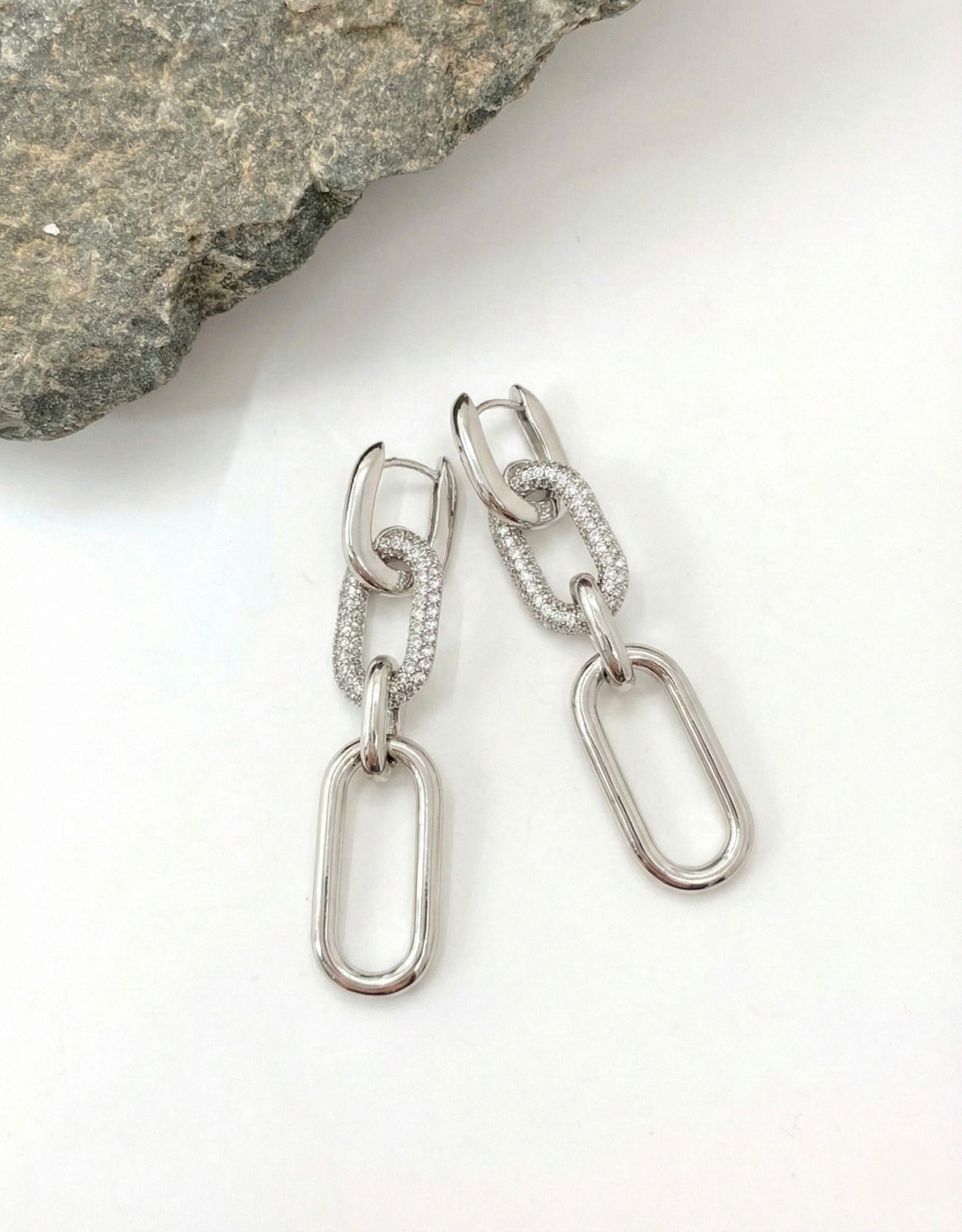 Silver chain link drop earrings with micro-pavé crystal middle link on textured stone surface