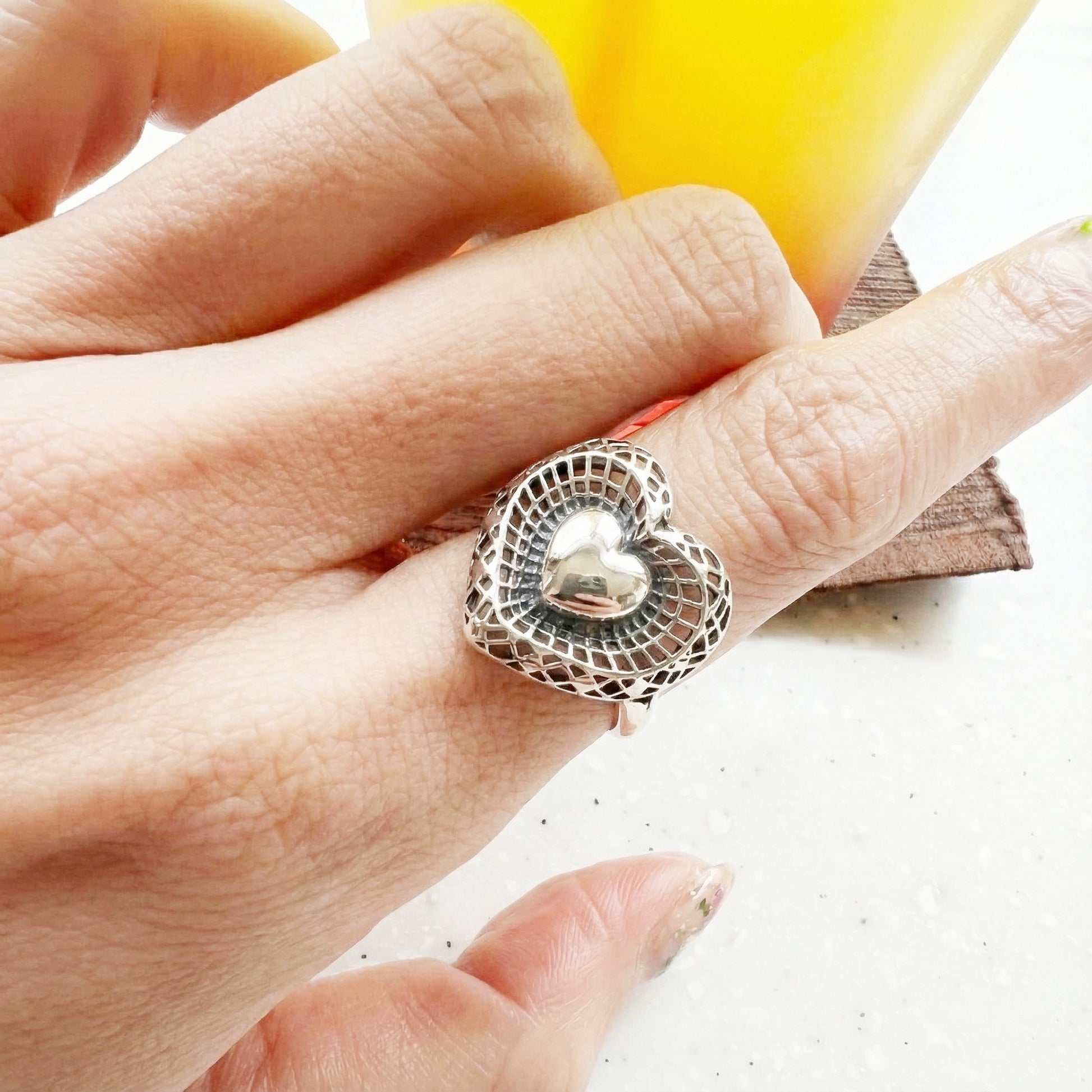 : Close-up of 925 silver filigree heart ring on middle finger showing detailed lattice texture and dimensional heart
