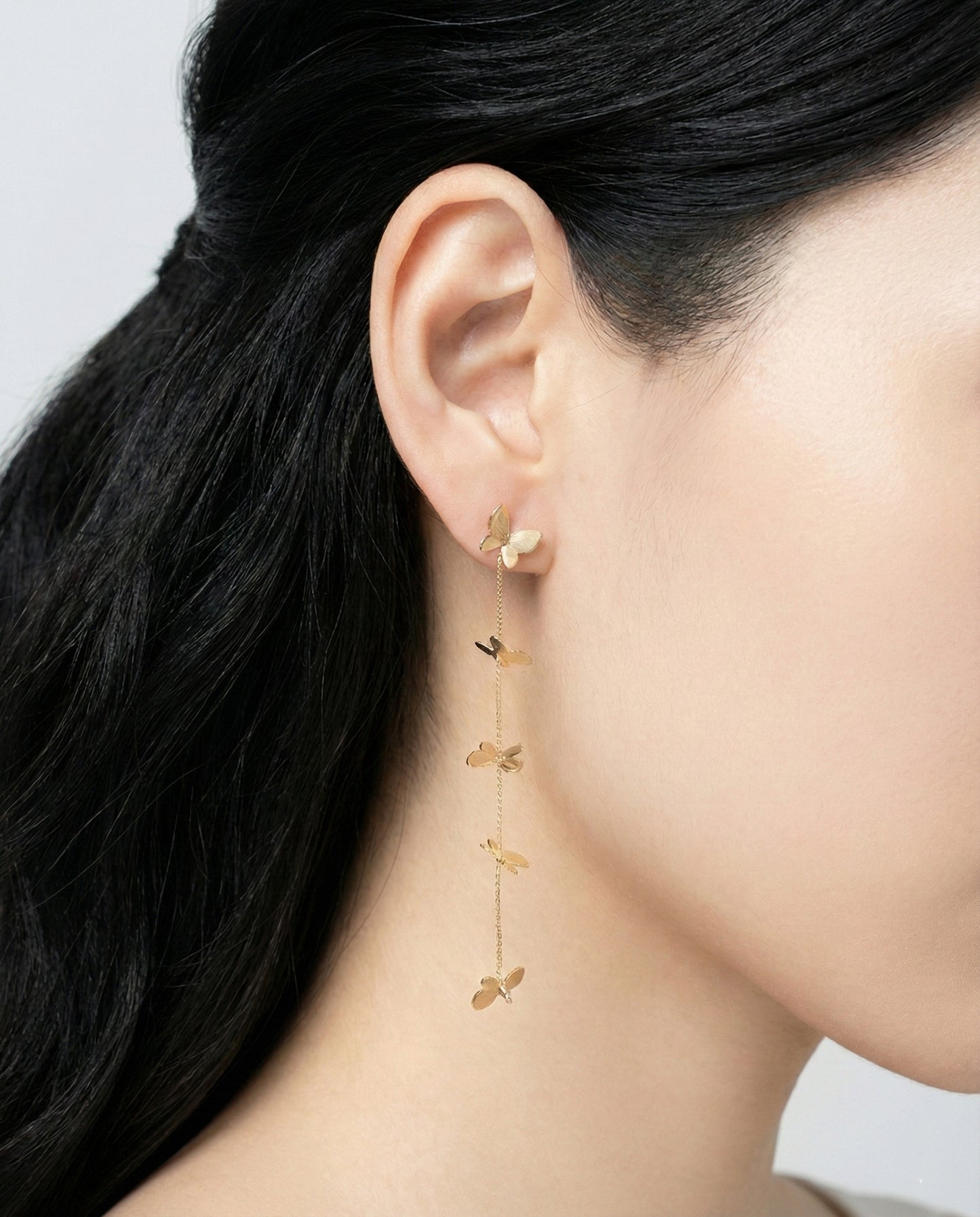 Gold butterfly long drop earrings with chain on model's ear profile view