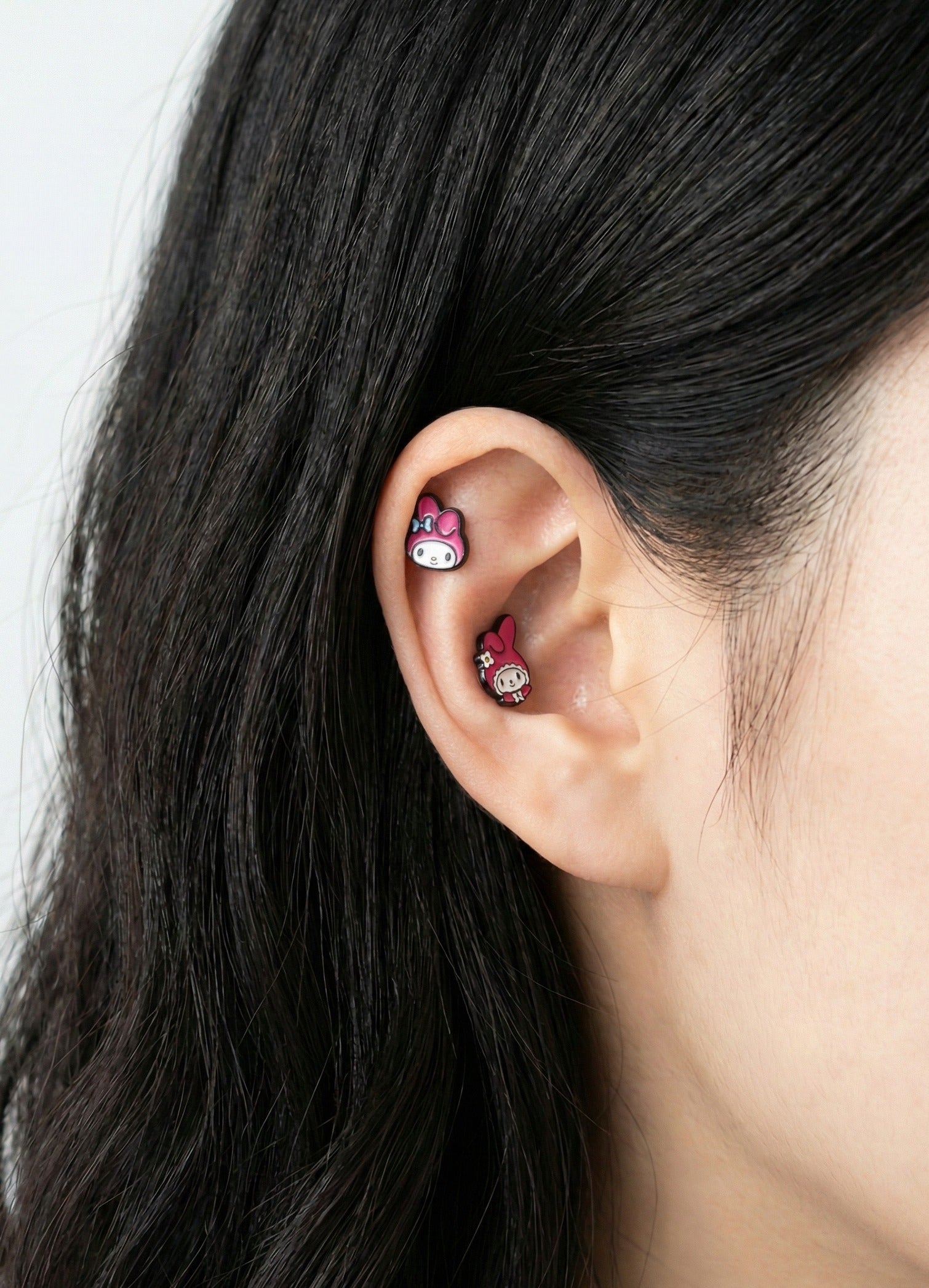 Close-up of My Melody character earrings layered on ear cartilage and lobe