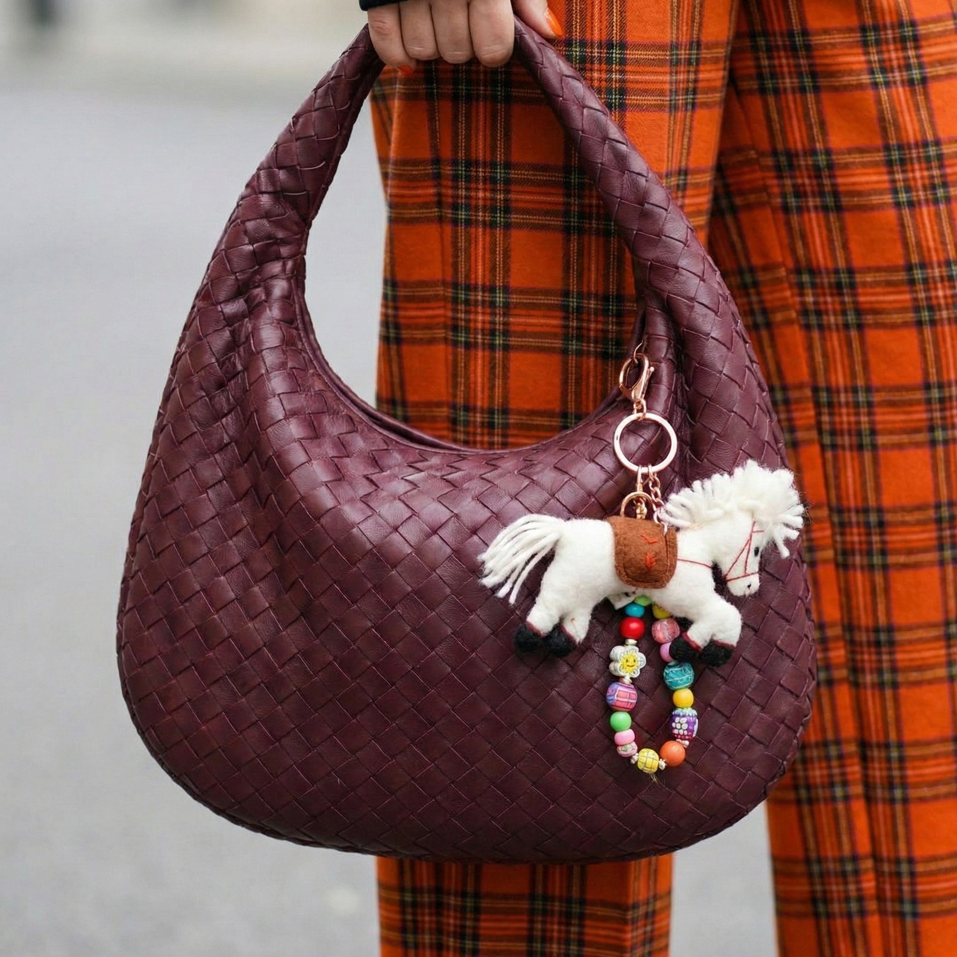White wool felt pony keychain on burgundy woven hobo bag with plaid skirt outfit